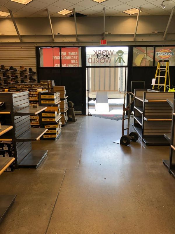unnamed Retail store being cleared out by a professional moving company, with empty shelves, stacked boxes, a dolly, and a ramp leading to a moving truck.